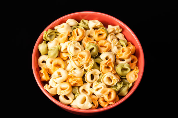 Colored tortellini, ring-shaped pasta in red bowl, black background