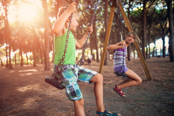 Two kids are swinging on a swing in pine forest.on tuscanian coast near Cecina. Italy, Tuscany. Sunny summer evening.