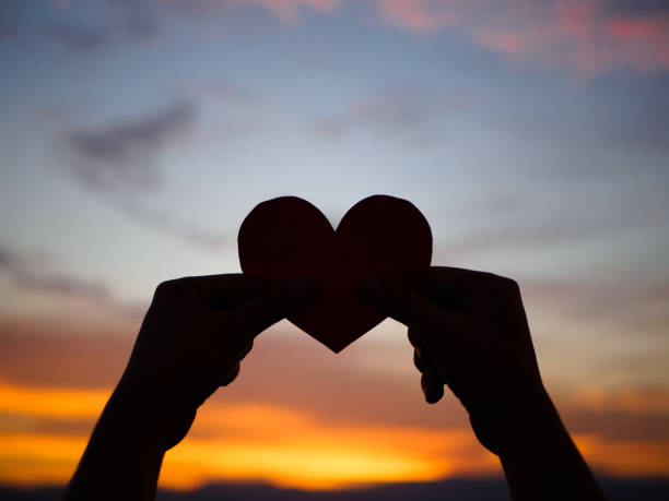 istock silhouette hand is raising the red paper heart with blur sunlight during sunset, 665333914