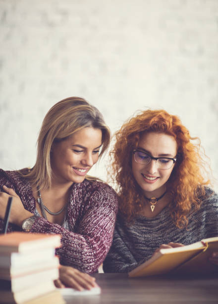 istock Two smiling female friends reading a book together. 665345688