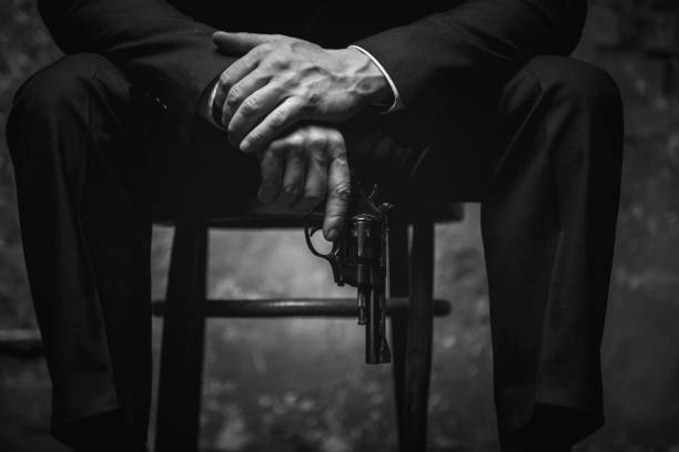 Wicked man holding his gun at the ready Better not irritate me. Dangerous aggressive mighty man sitting on a chair wearing stylish suit and blackmailing his business rival organized crime photos stock pictures, royalty-free photos & images