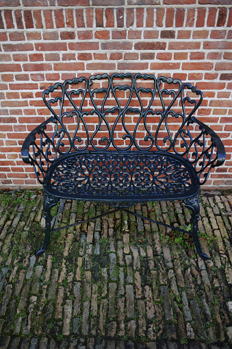 Decorative wrought iron bench in the garden near old brick wall