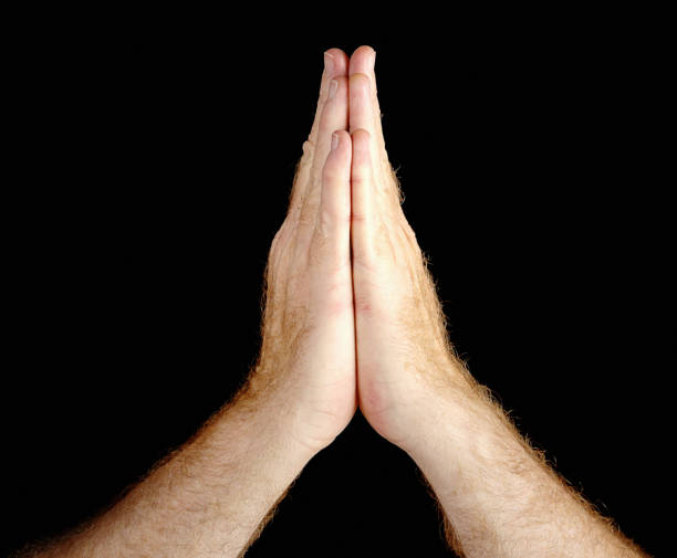 istock Hand signs: male hands clasped in prayer against black background 665404886