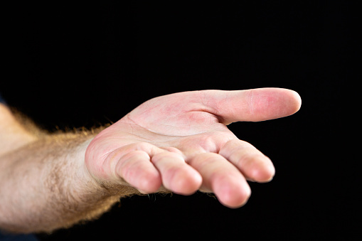 A man's hand is held out, palm up, giving, taking, or begging, against a black background with some copy space.