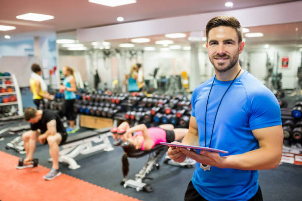 Handsome trainer using tablet in weights room stock photo