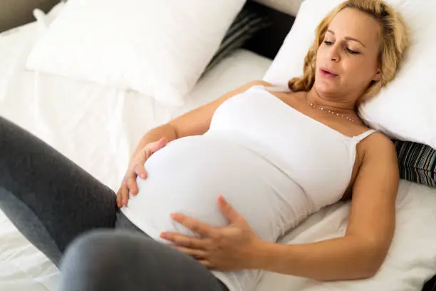 Pregnantwoman lying ill in bed with contractions