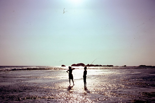 Mannar Island, Sri Lanka - November 5, 1980: Two fishermen are standing on the beach of Mannar Island at the sunset. Fishing is one of the most important activity in Sri Lanka.