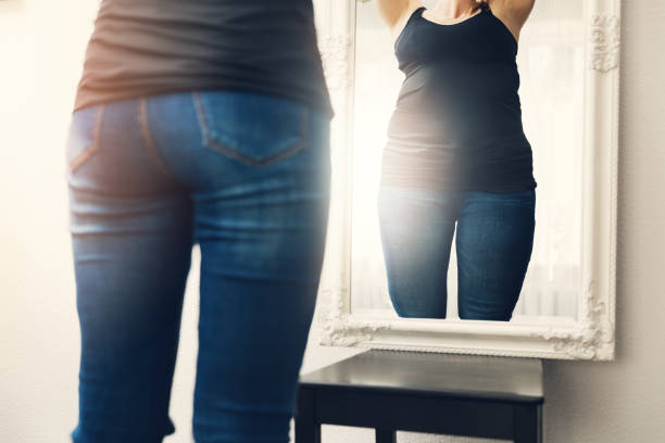 concetto di anoressia - la donna guarda il suo riflesso grasso nello specchio - pantaloni aderenti foto e immagini stock