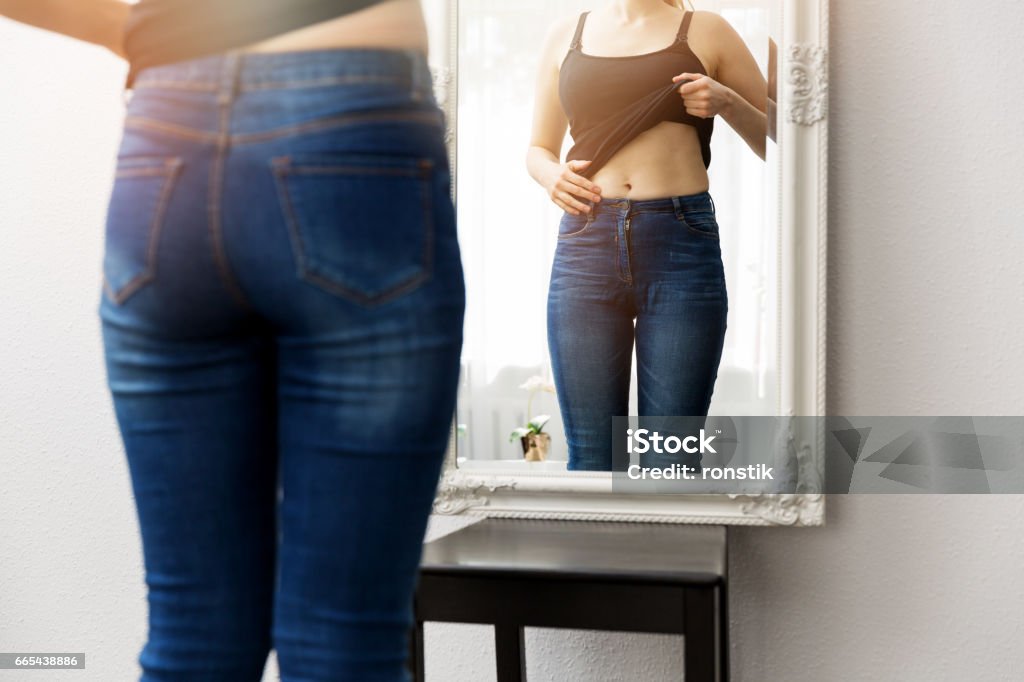 donna che controlla il suo corpo davanti allo specchio - Foto stock royalty-free di Specchio