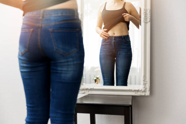 donna che controlla il suo corpo davanti allo specchio - cura del corpo foto e immagini stock