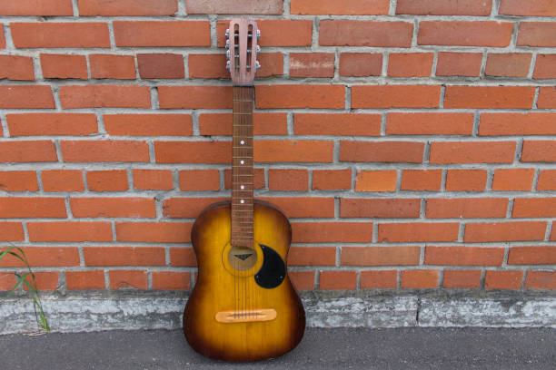 istock Acoustic guitar resting against a red brick wall 665444340