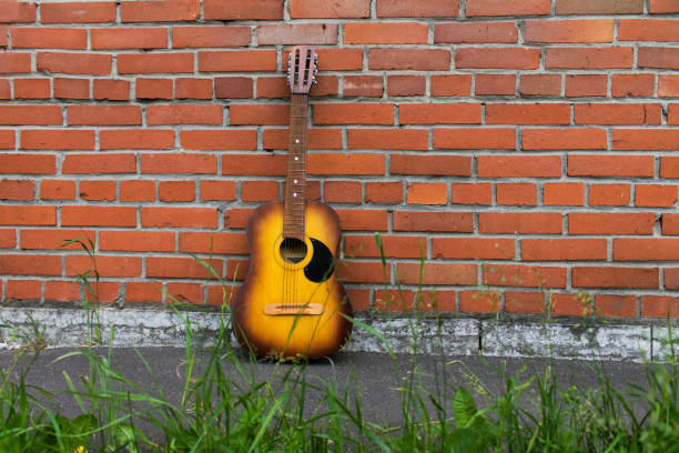 istock Acoustic guitar resting against a red brick wall 665444366