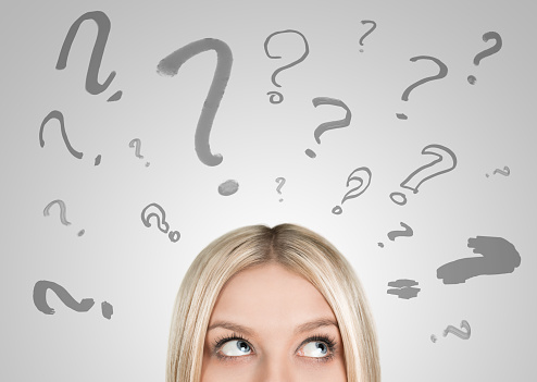 Close up of blonde woman looking upwards on many question marks with copy space