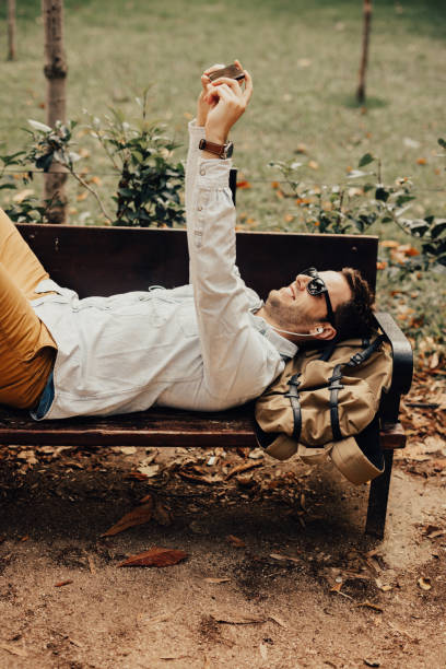 istock Beautiful man taking a selfie in the park while lying on the bench 665471412