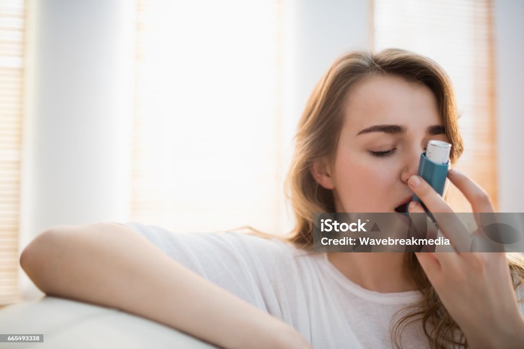 Woman using her inhaler on couch Woman using her inhaler on couch in the living room Asthmatic Stock Photo