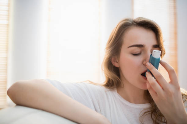 Woman using her inhaler on couch stock photo