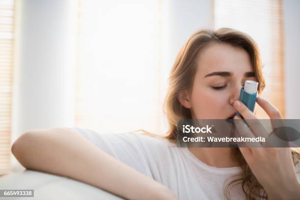 Woman Using Her Inhaler On Couch Stock Photo - Download Image Now - Asthmatic, Asthma Inhaler, Women