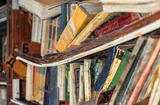 The bent shelf with old dampened books in an abandoned library. Focus on the center of the frame, shallow depth of field