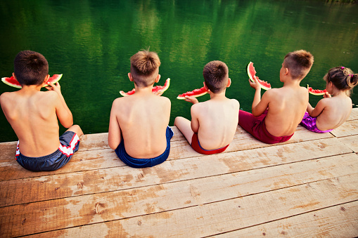 summer time, children sitting on a deck overlooking river, eating watermelon