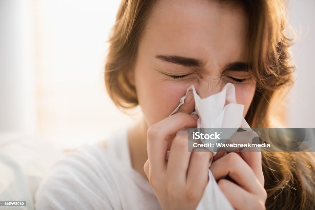 Woman blowing her nose on couch Woman blowing her nose on couch in the living room Sneezing Stock Photo