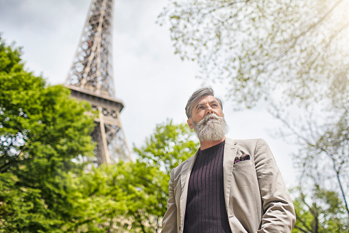 Low angle view of businessman looking away by Eiffel Tower. Confident senior professional is wearing jacket. Handsome male is standing against sky.