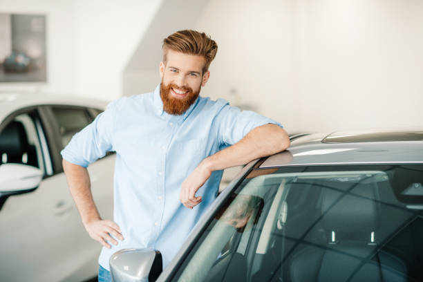 istock Handsome bearded young man standing with new car in auto salon 665524286