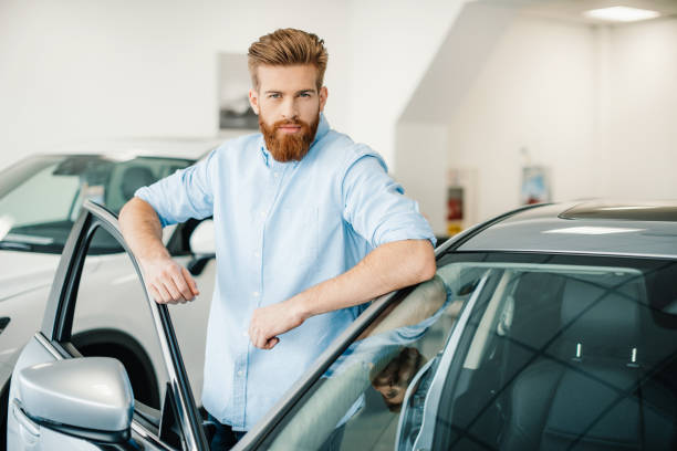 istock Handsome bearded young man standing with new car in auto salon 665524426