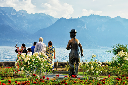 Vevey, Switzerland - August 27, 2016: People at Charlie Chaplin statue at Geneva Lake in Vevey, Vaud canton in Switzerland. Alps mountains on the background