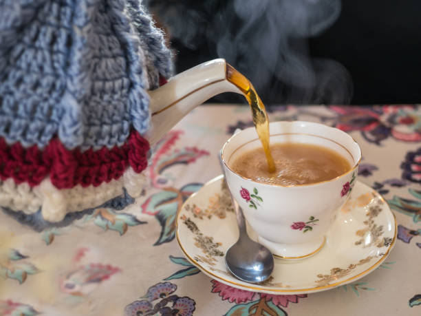istock Tea being poured form a vintage tea pot, cosy or cozy and tea cup. 665533504