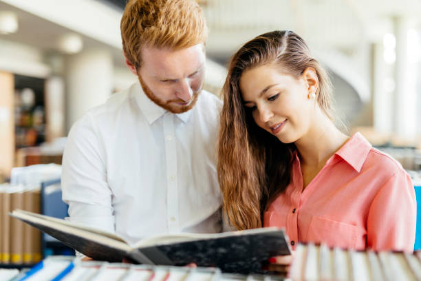 istock Two  smart students reading and studying in library whole searching through books on the shelves 665536042