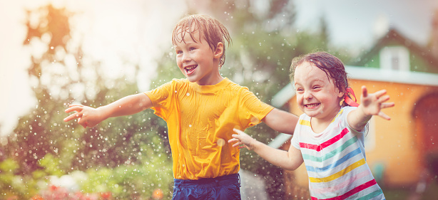 Sister and brother jumping through spray at back yard in summer