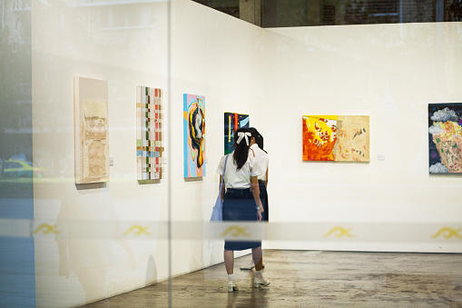 Young woman in the art gallery looking at paintings, abstract contemporary art concept