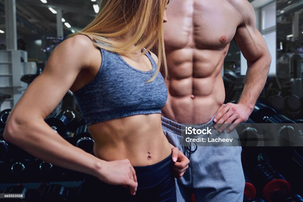 Strong man and a woman are posing with beautiful bodies. Strong man and a woman are posing with beautiful bodies. Sports couple in the gym. Couple - Relationship Stock Photo