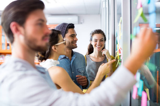 istock Smiling executives writing on sticky notes on glass wall 665553664