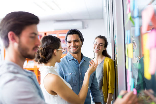 istock Smiling executives discussing over sticky note on glass wall 665554834