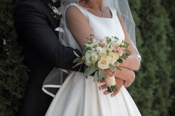 istock bride holds a wedding bouquet in hands, the groom hugs her from behind 665570366