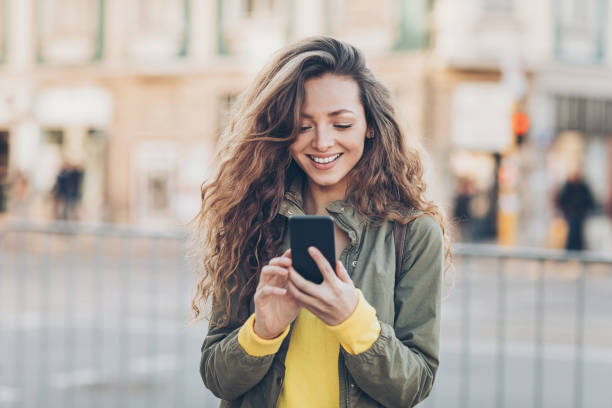 Beautiful girl texting on the street Young woman with smart phone texting outdoors in the city pretty girl smiling stock pictures, royalty-free photos & images