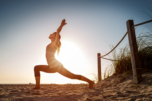 Woman performs stretching exercises on a beach at sunrise