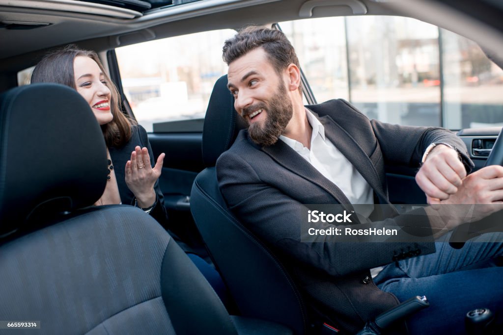 Business couple in the car Businesswoman on the backseat with elegant man driving a car in the city. Worried about a delay to an important meeting Taxi Driver Stock Photo