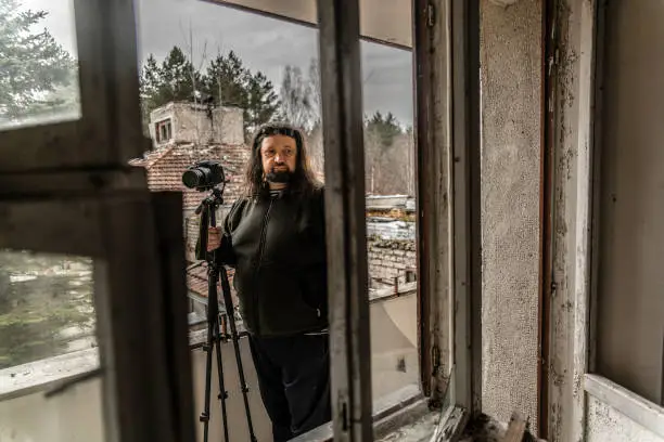Photo of Mature man, 50 years old Caucasian with the beard and long hairs, photographer, shooting abandoned resort in Belarus