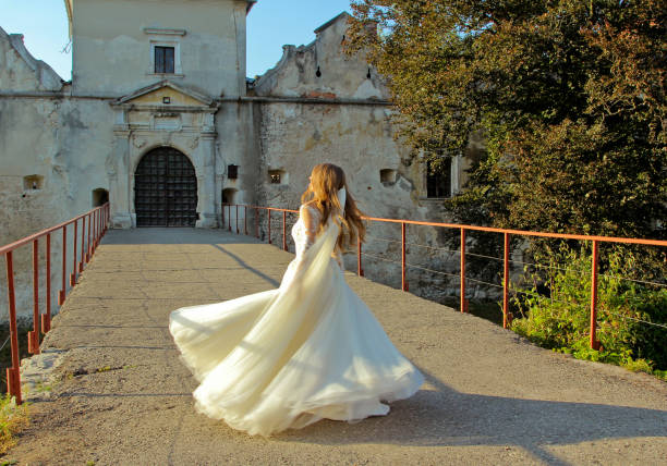 Girl walking in oldest Svirz Castle in Ukraine. Bride veil and drees beauty fading away