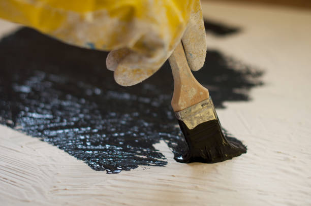 istock hand in yellow glove paints a black surface with white stone 665637734