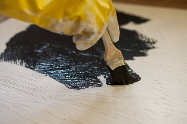 istock hand in yellow glove paints a black surface with white stone 665643838