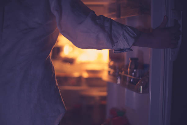 primo-up della donna che tiene la porta del frigorifero aperta durante la notte - ingordigia foto e immagini stock
