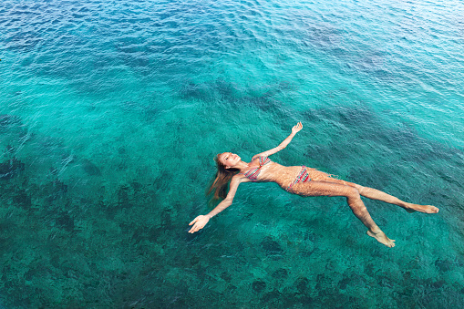 Young slim woman lie on back and relaxing in blue sea water