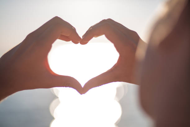 istock Silhouettes hand heart shaped with sunset and sea background 665659832