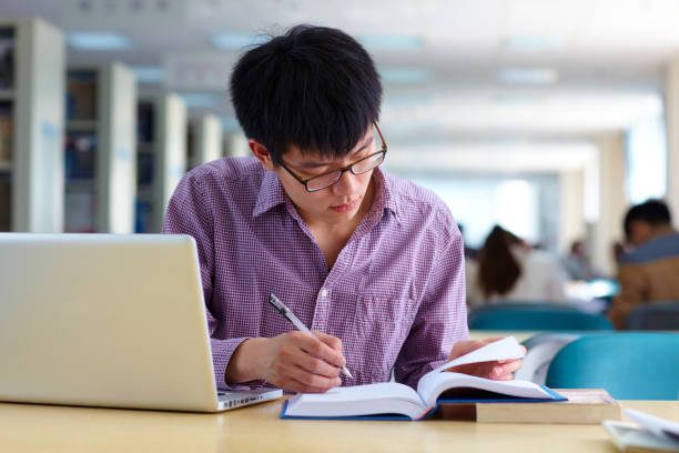 istock One male asian college student study in the library with laptop on table 665660266