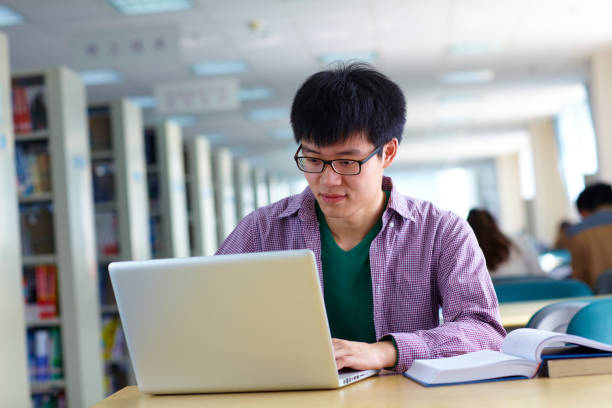 istock One male asian college student study in the library with laptop on table 665660270