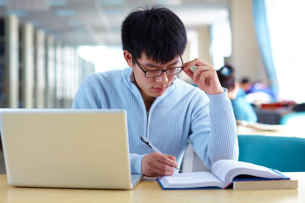 istock One male asian college student study in the library with laptop on table 665660280