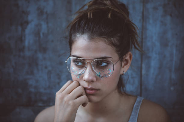 Portrait of a cute teenage girl posing against a gray background with glitter on her face.